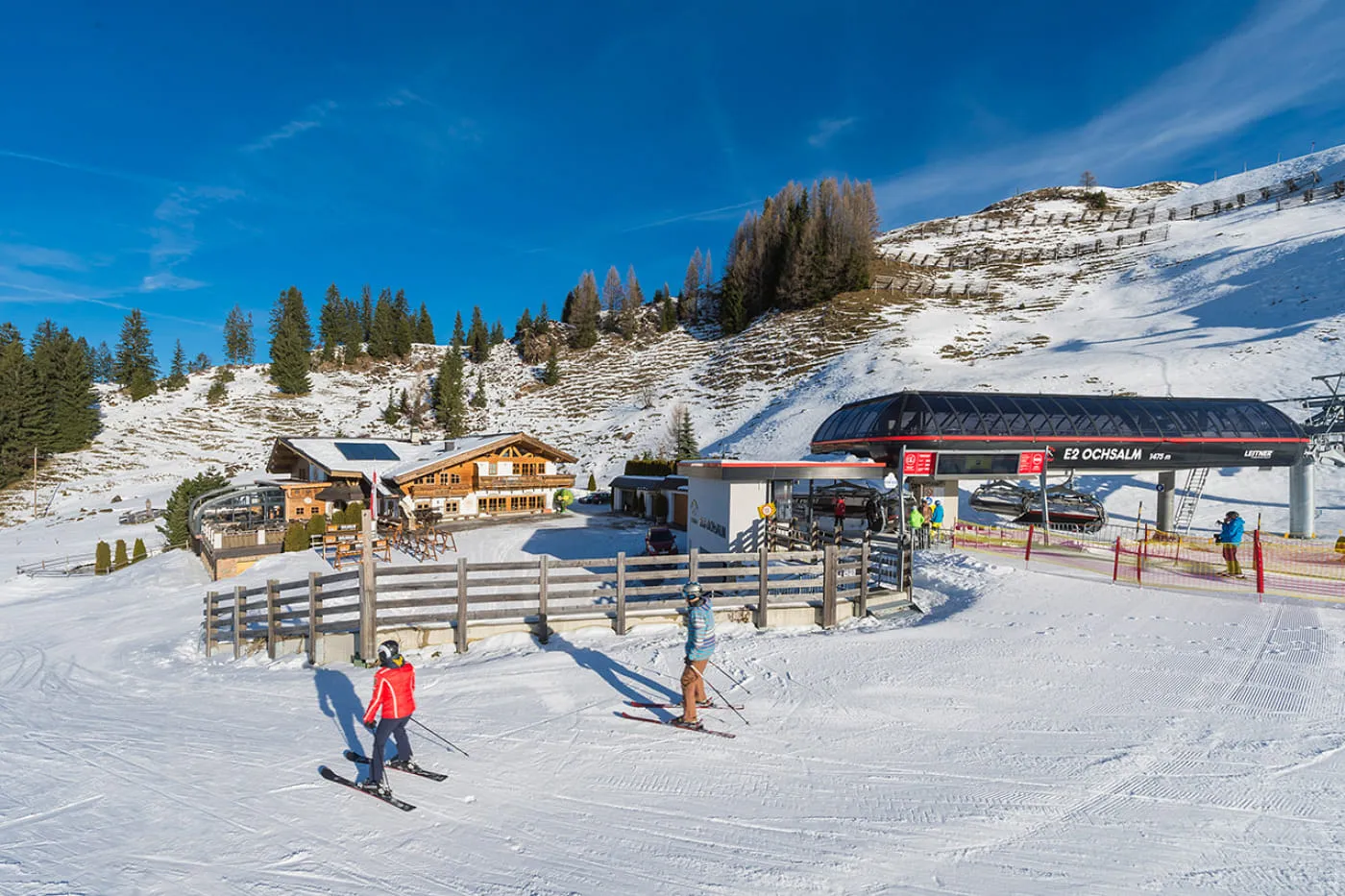 Verschneite OchsAlm neben der Sesselbahn E2 Ochsalm, zwei Skifahrer auf der präparierten Piste davor